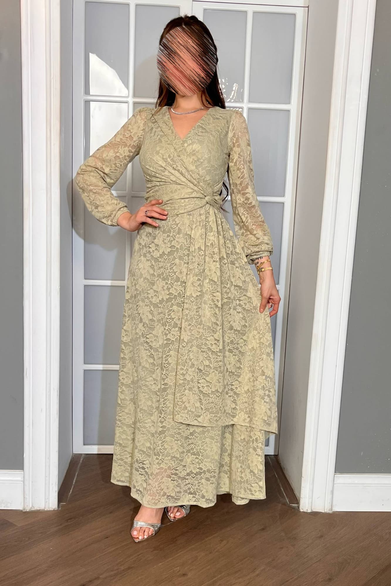 فستان طويل من الدانتيل بلون أخضر فاتح هادئ، يعكس أنوثة راقية ولمسة رومانسية ناعمة يتميّز بقصّة لفّ (Wrap) أنيقة مع عقدة جانبية تبرز الخصر