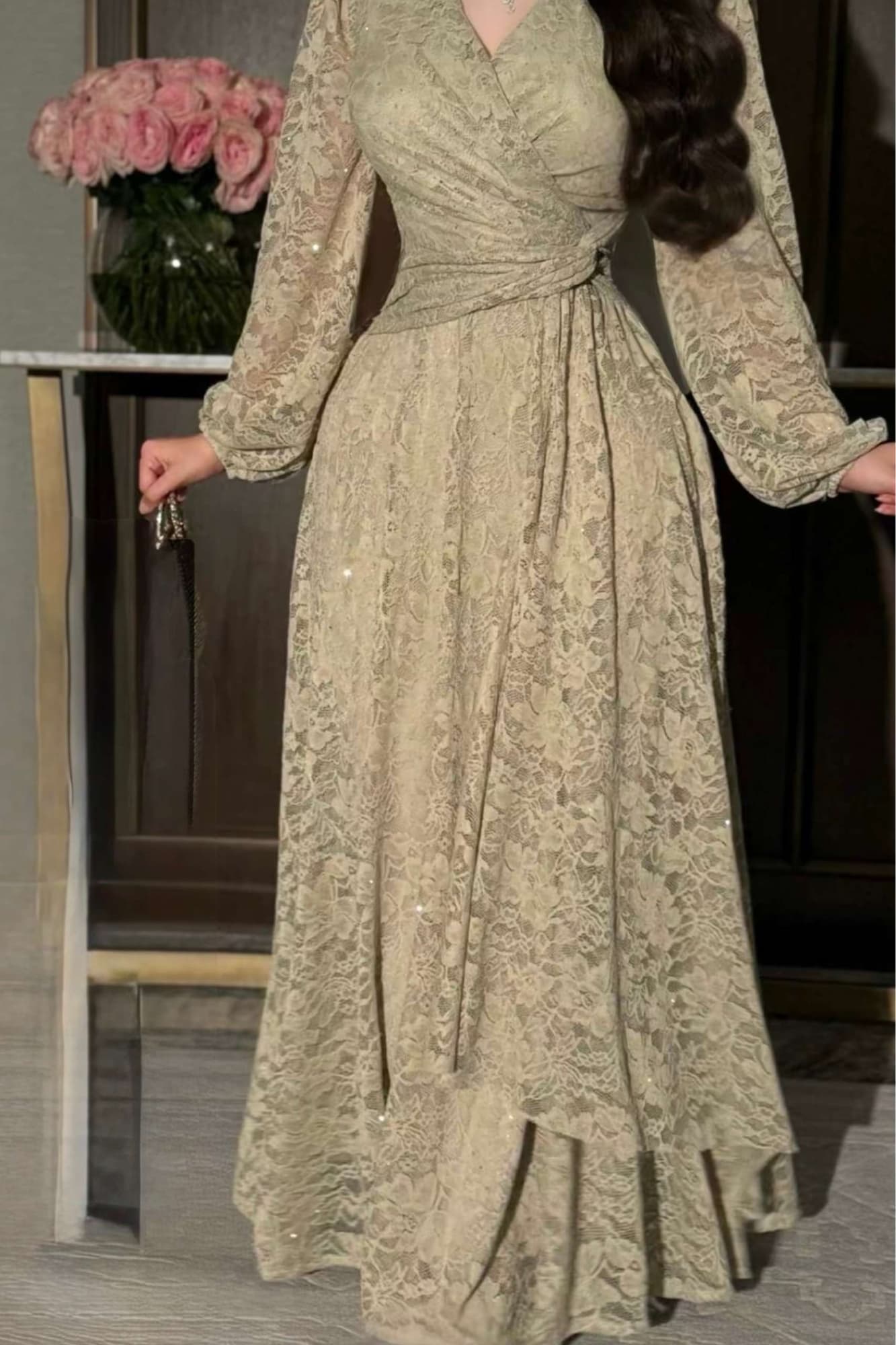 فستان طويل من الدانتيل بلون أخضر فاتح هادئ، يعكس أنوثة راقية ولمسة رومانسية ناعمة يتميّز بقصّة لفّ (Wrap) أنيقة مع عقدة جانبية تبرز الخصر عشبي