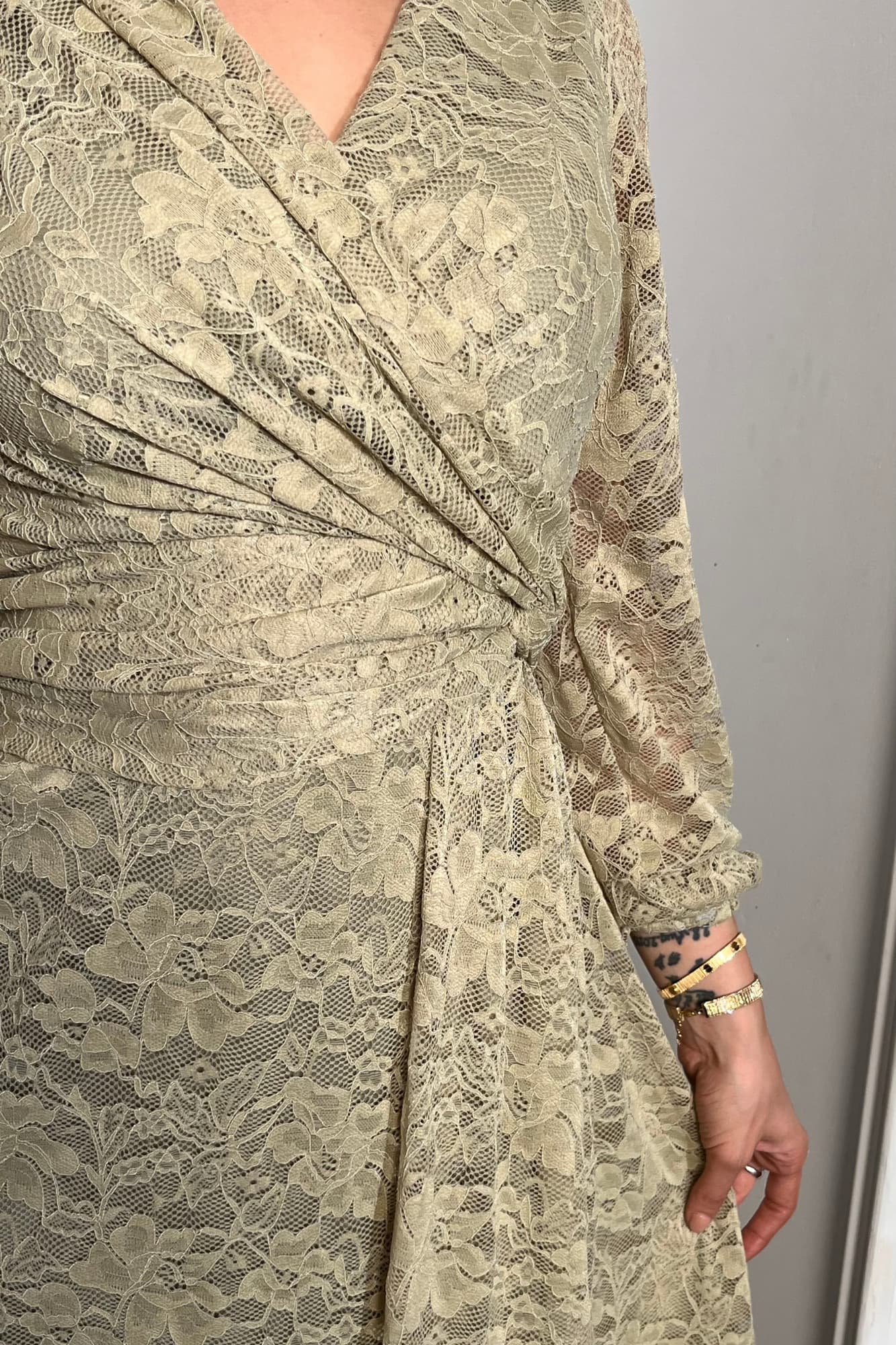 فستان طويل من الدانتيل بلون أخضر فاتح هادئ، يعكس أنوثة راقية ولمسة رومانسية ناعمة يتميّز بقصّة لفّ (Wrap) أنيقة مع عقدة جانبية تبرز الخصر عشبي