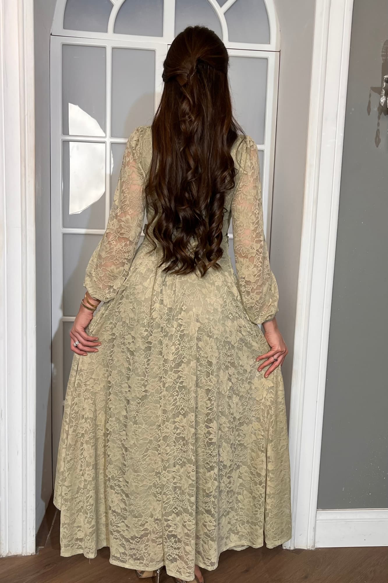 فستان طويل من الدانتيل بلون أخضر فاتح هادئ، يعكس أنوثة راقية ولمسة رومانسية ناعمة يتميّز بقصّة لفّ (Wrap) أنيقة مع عقدة جانبية تبرز الخصر