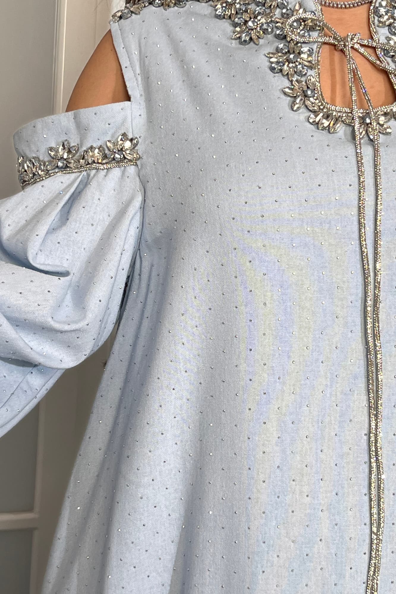 فستان طويل يتميّز بقصّة واسعة مريحة تنسدل بانسيابية أنثوية مع أكمام طويلة مفتوحة عند الكتفين تضيف لمسة عصرية راقية. سماوي