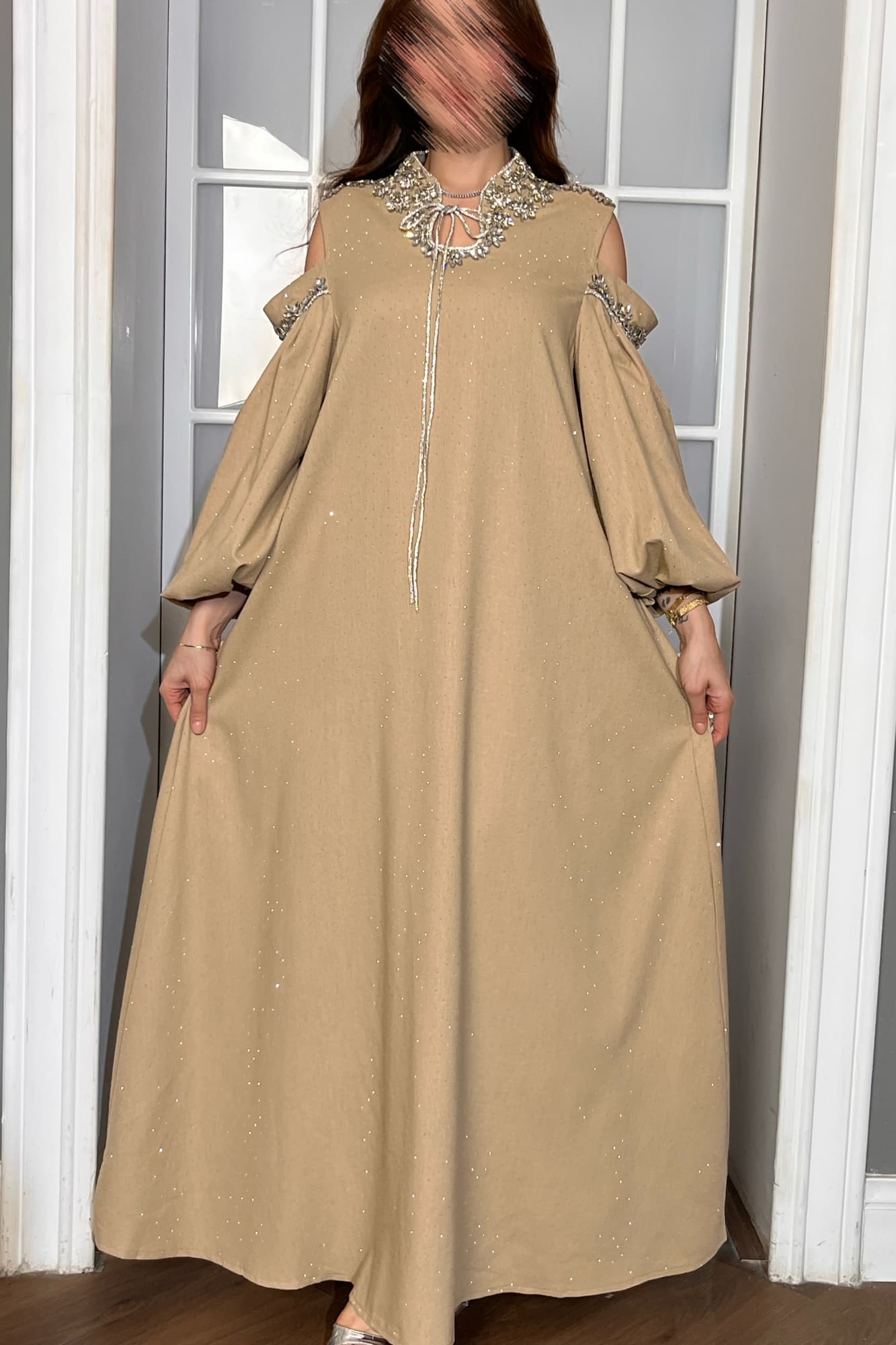 فستان طويل يتميّز بقصّة واسعة مريحة تنسدل بانسيابية أنثوية مع أكمام طويلة مفتوحة عند الكتفين تضيف لمسة عصرية راقية.