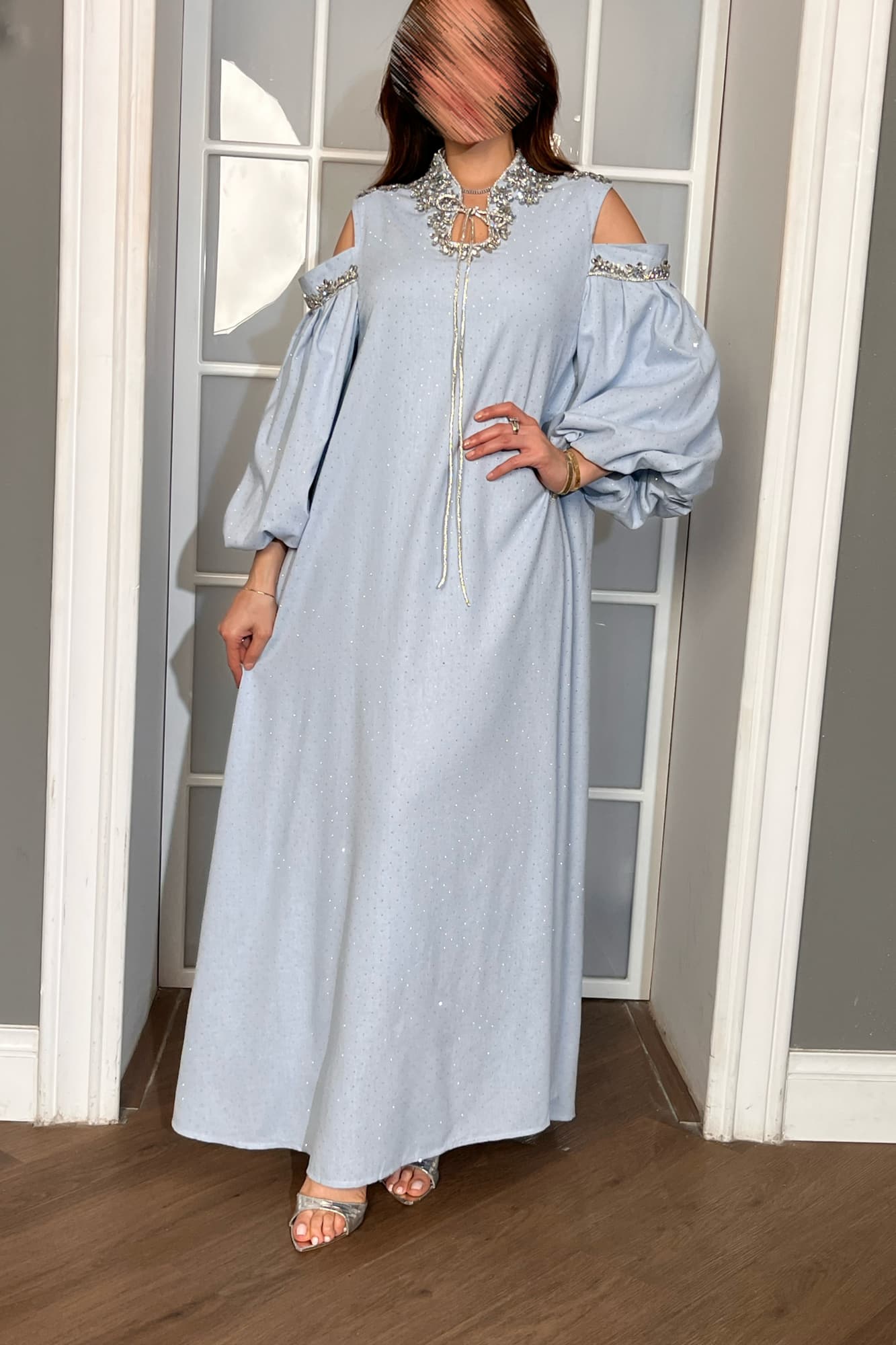 فستان طويل يتميّز بقصّة واسعة مريحة تنسدل بانسيابية أنثوية مع أكمام طويلة مفتوحة عند الكتفين تضيف لمسة عصرية راقية.