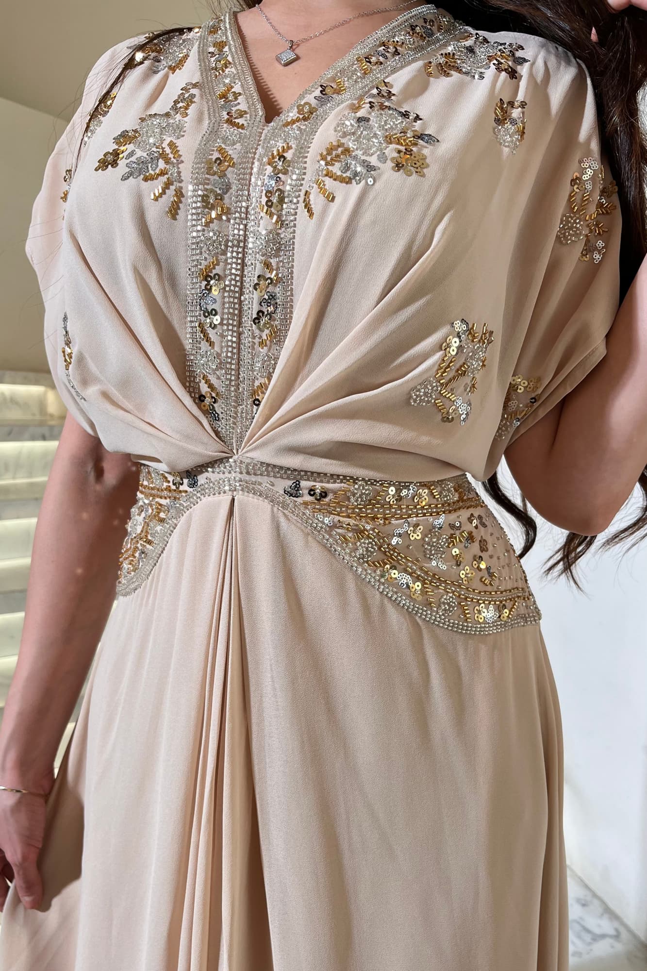 جلابية أنيقة مزينة بتطريز يدوي من خيوط ذهبية وكريستالات لامعة تضيف لمسة فخمة بدون مبالغة بيج