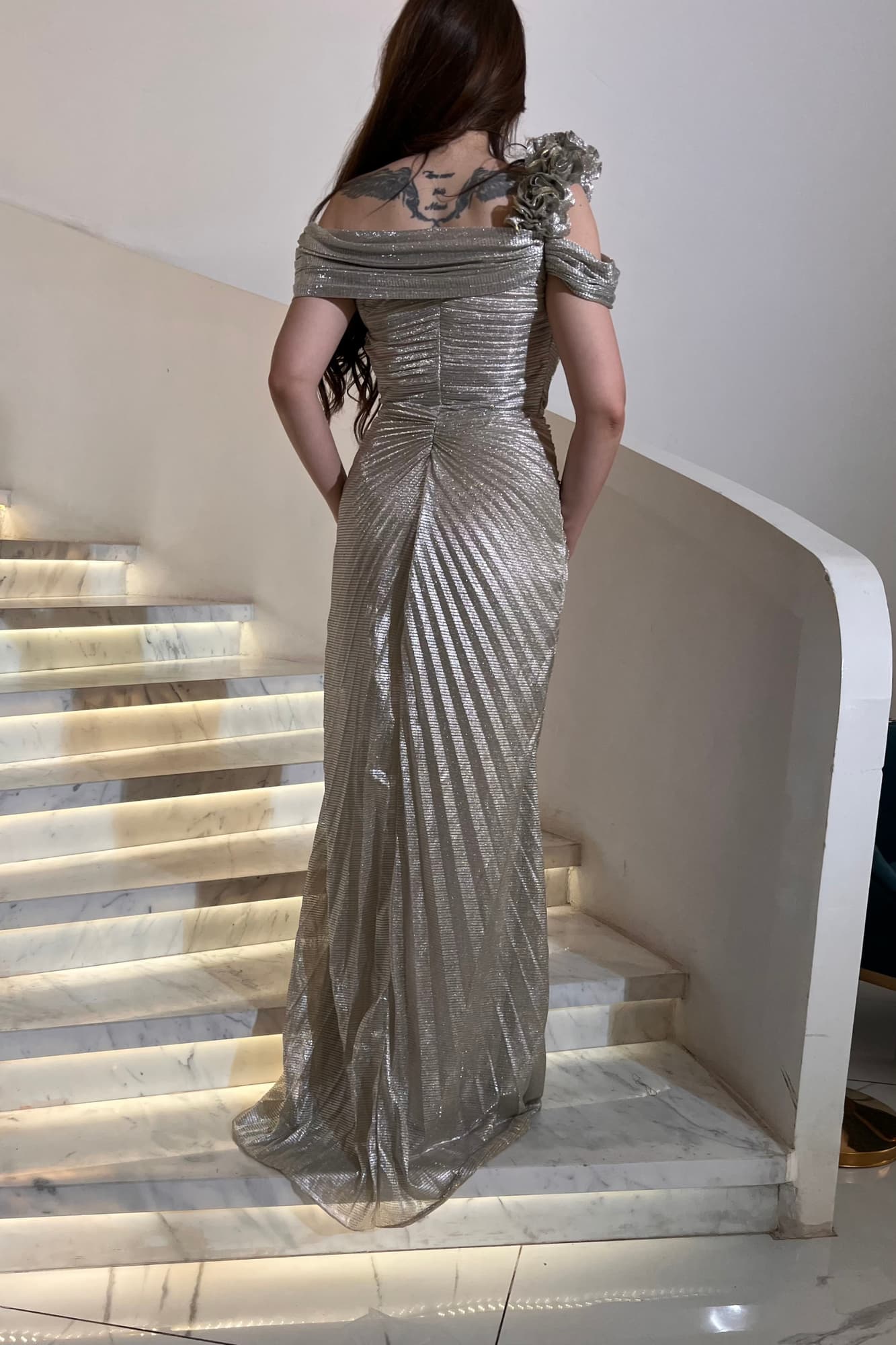 فستان فضّي بتصميم انسيابي يبرز جمال القوام بطريقة راقية من قماش لمّاع مُكسر