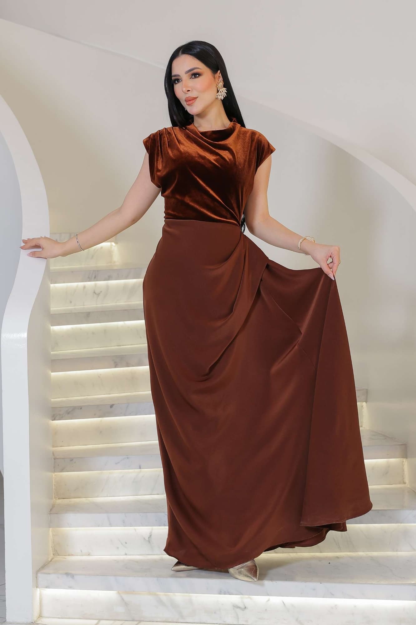 فستان يجمع بين نعومة المخمل في الجزء العلوي وانسيابية قماش الساتان في الاسفل ليخلق تباينًا غنيًا بالفخامة والأنوثة.