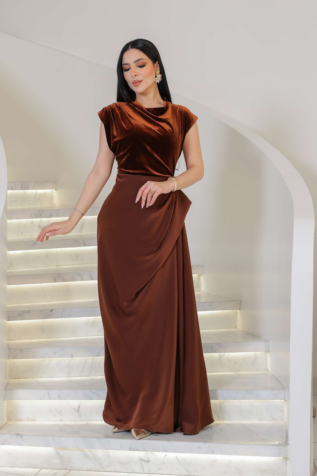 فستان يجمع بين نعومة المخمل في الجزء العلوي وانسيابية قماش الساتان في الاسفل ليخلق تباينًا غنيًا بالفخامة والأنوثة.