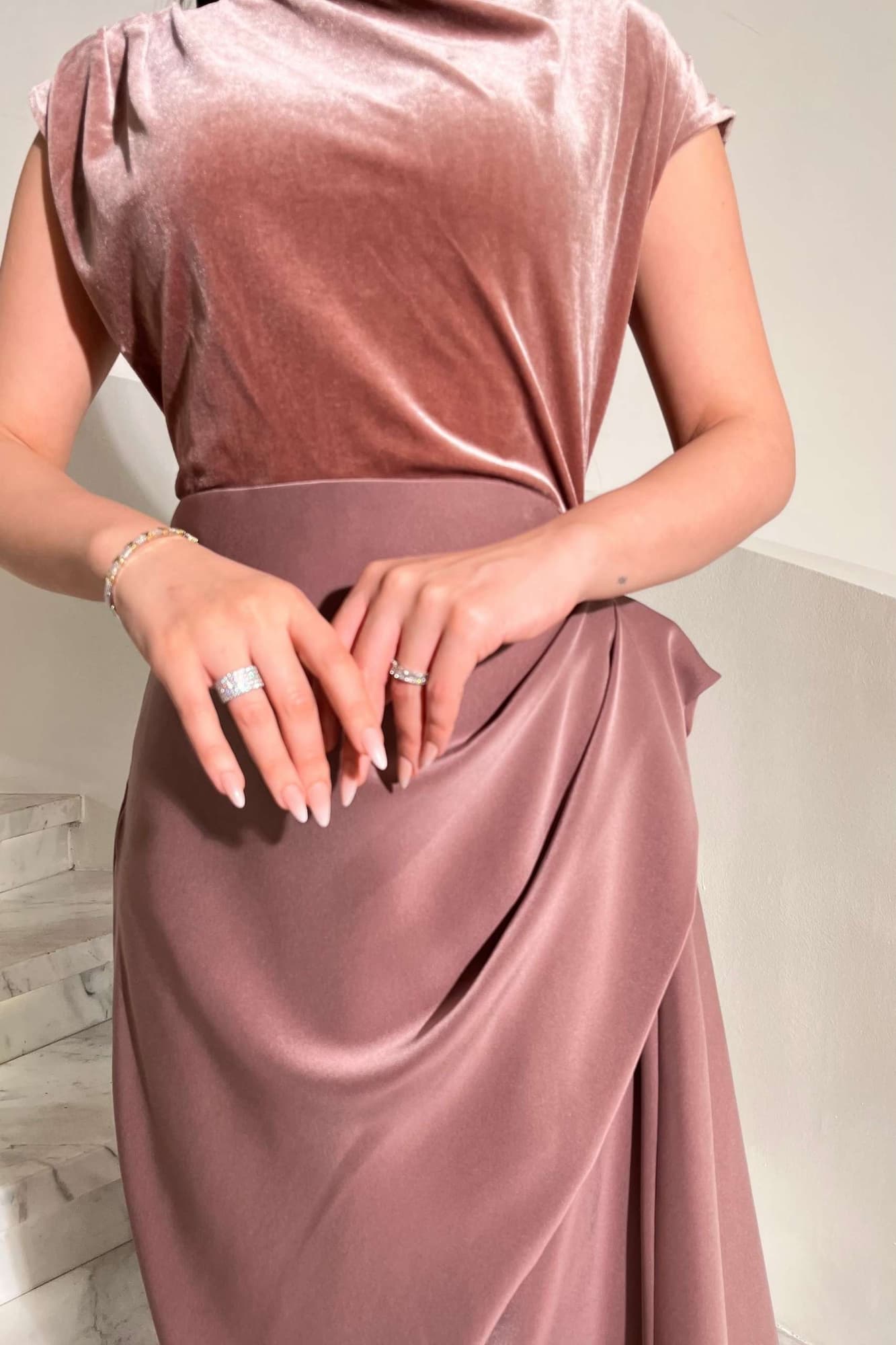 فستان يجمع بين نعومة المخمل في الجزء العلوي وانسيابية قماش الساتان في الاسفل ليخلق تباينًا غنيًا بالفخامة والأنوثة لحمي