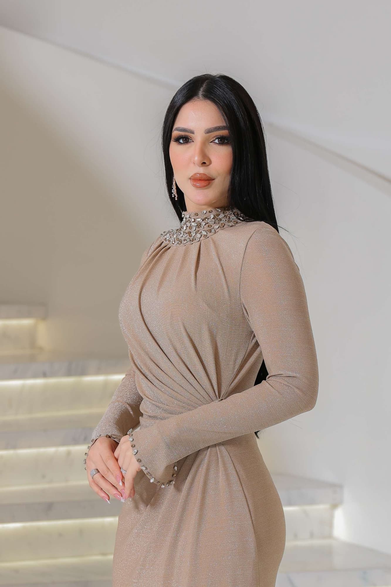 فستان طويل يجسّد الفخامة الهادئة، بلون بيج دافئ بلمعة ناعمة تعكس الضوء برقي