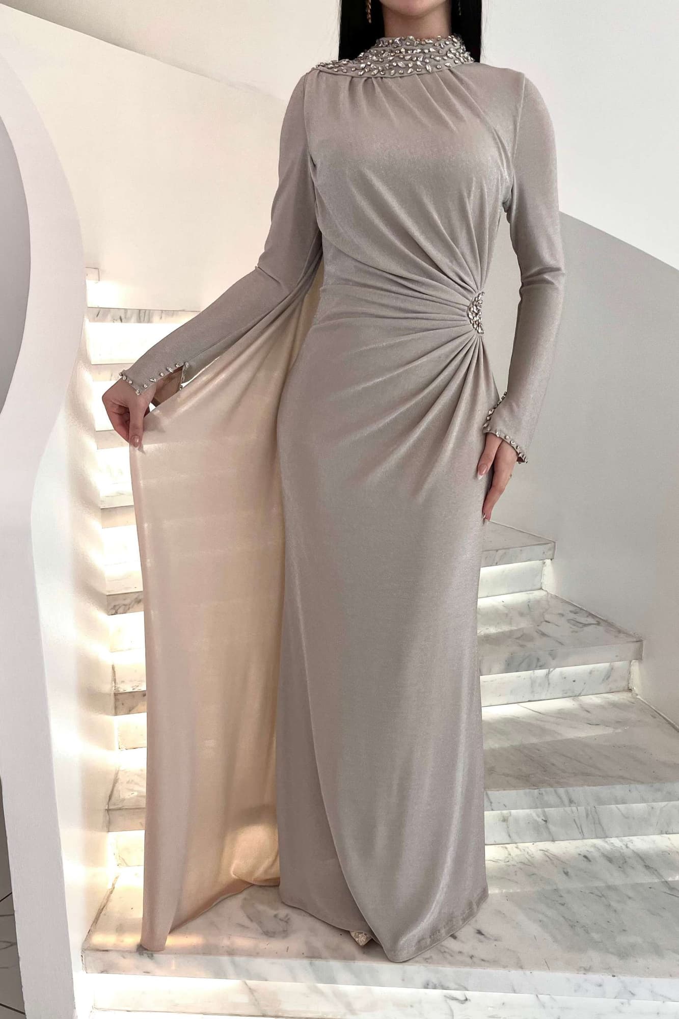 فستان طويل يجسّد الفخامة الهادئة، بلون بيج دافئ بلمعة ناعمة تعكس الضوء برقي